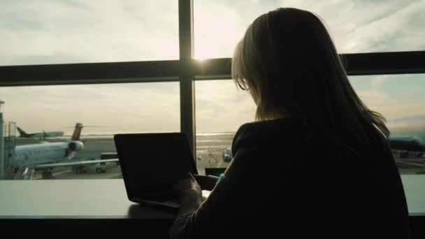 Женщина использует ноутбук в аэропорту. За окном вы можете увидеть самолеты — стоковое видео