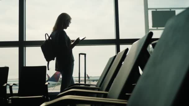 Geschäftsfrau wartet auf einen Flug. am Fenster stehen und ein Tablet benutzen — Stockvideo