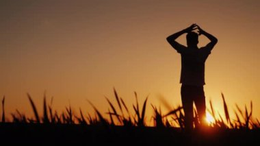 Siluet bir genç adam temiz hava sahiptir ve gün batımı hayran. Ellerini başının arkasına tutar, ileride onun önünde görünüyor