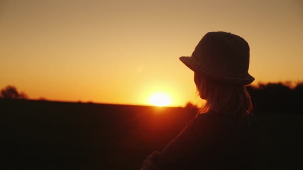 Una mujer con sombrero espera la puesta del sol. Esperanza y brillante concepto de futuro — Vídeo de stock