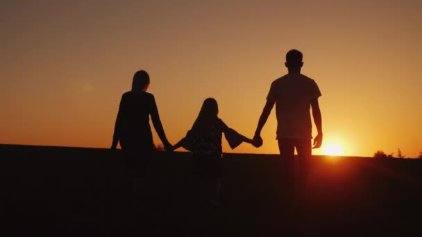 Les parents avec l'enfant avancent vers le coucher du soleil. Silhouettes familiales. Steadicam shot — Video