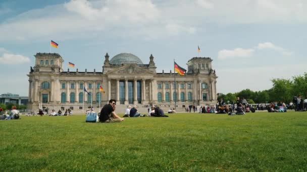 Berlin, Tyskland, maj 2018: Turister och lokalbefolkning vila på en grön gräsmatta nära byggnaden av förbundsdagen i Berlin — Stockvideo