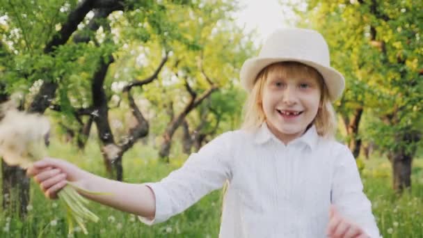 Un bambino felice sta correndo felicemente attraverso il giardino, rimbalzando e agitando un mazzo di denti di leone. Concetto di infanzia spensierata — Video Stock