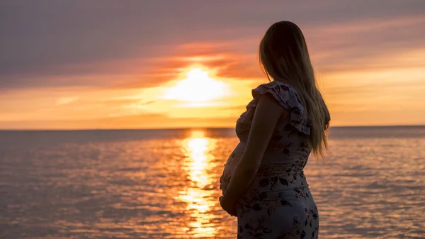 Mulher grávida olha para o pôr do sol sobre o mar — Fotografia de Stock