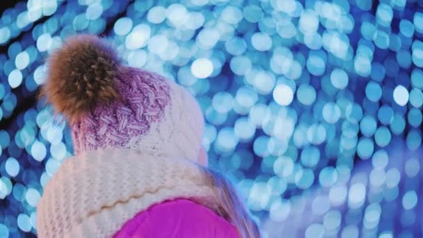 Chica mira las luces azules de guirnaldas, decoración para Navidad y Año Nuevo — Vídeos de Stock