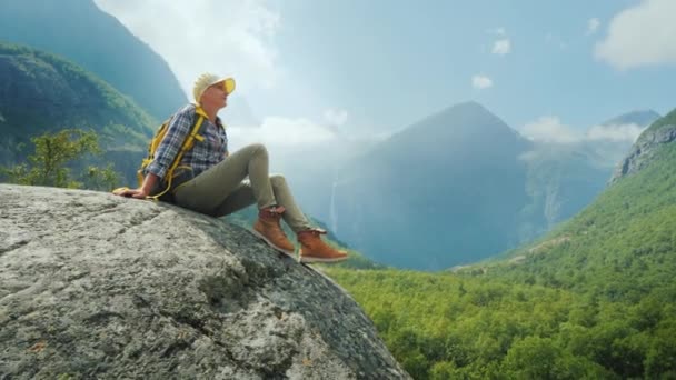 El turista se sienta en una gran roca rodeada de altas montañas. Sola en medio de la naturaleza increíblemente hermosa de Noruega — Vídeo de stock