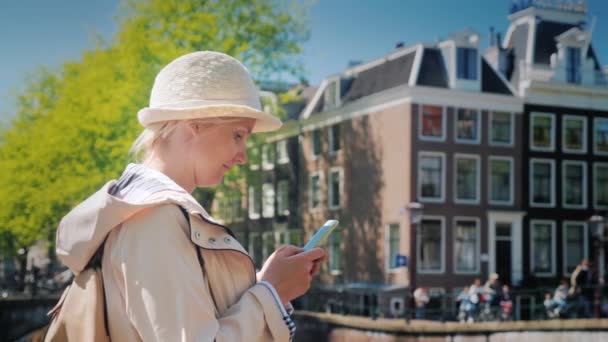 Mujer joven utiliza un teléfono inteligente en un puente sobre un canal en Amsterdam — Vídeo de stock