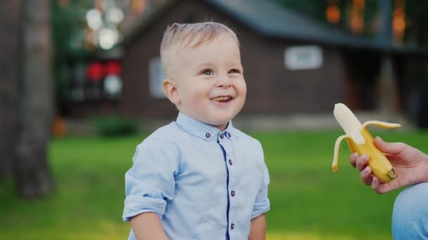 Joyeux bébé mange une banane que sa mère lui donne — Video