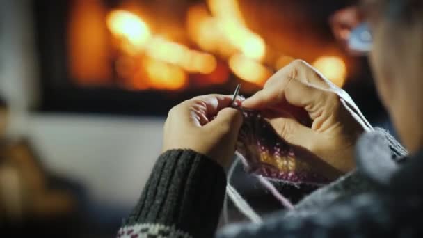 Gros plan des mains d'une femme âgée qui tricote une chose terne sur le fond de la cheminée — Video