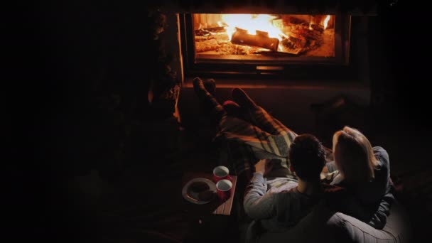 Egy fiatal pár csodálja a tüzet a kandallóban, mellettük ülnek és teát isznak.. — Stock videók