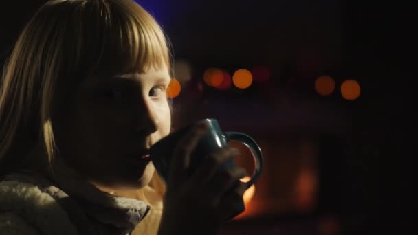 Mädchen trinkt Tee sitzend am Fenster, ein Kamin und ein Weihnachtsbaum werden von hinten angezündet — Stockvideo