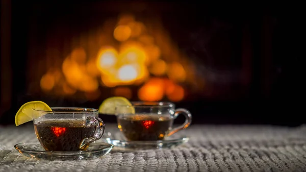 Two cups of tea with lemon on the background of the fireplace. Stand on a white knitted tablecloth — Stock Photo, Image