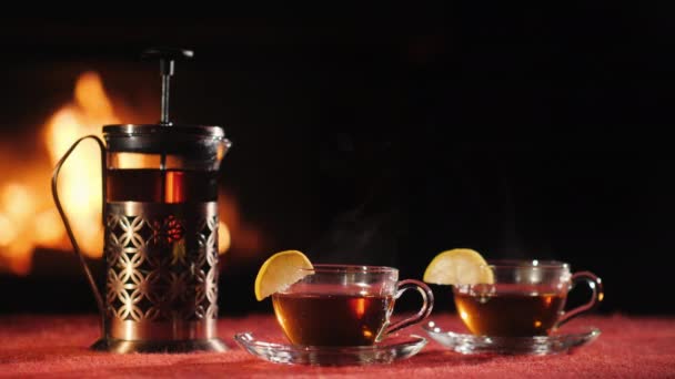 A teapot and two glass cups with tea stand on a table against the background of the fireplace where the fire is burning — Stock Video