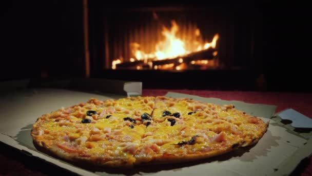 Pizza en una caja de cartón sobre la mesa sobre el fondo de la chimenea — Vídeo de stock