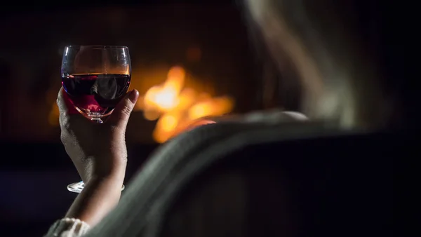 Вид ззаду Жінка п'є червоне вино, сидячи біля каміна, вид ззаду — стокове фото
