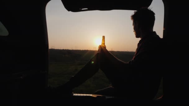 Bir genç bir arabanın bagajında oturur ve bir şişeden bira içer. — Stok video