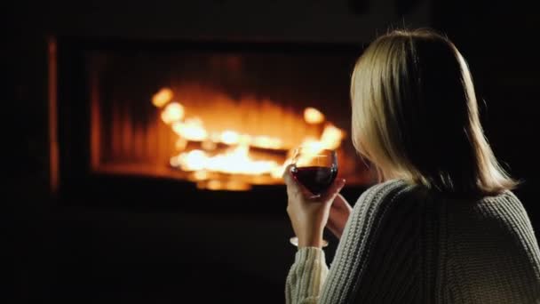 Mujer bebiendo vino tinto mientras está sentado junto a la chimenea, vista trasera — Vídeo de stock