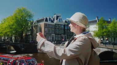 Genç bir kadın Amsterdam 'da kanal kenarında selfie çekiyor.