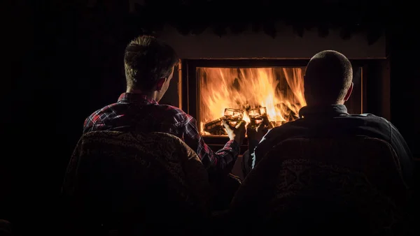 Dois homens bonitos descansam junto à lareira, bebendo brandy lentamente — Fotografia de Stock