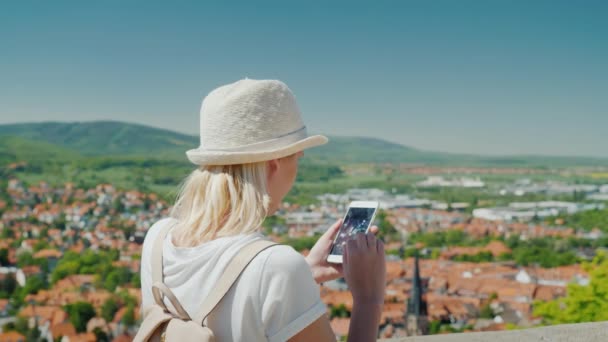 山の中の美しいヨーロッパの町を背景にスマートフォンを持つ女性。ヨーロッパの観光と旅行、通信とローミングの概念 — ストック動画