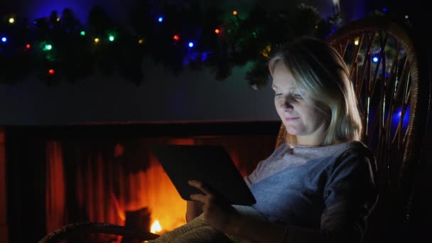 Retrato de mulher usa uma tabuleta contra o fundo de uma lareira e guirlandas festivas — Vídeo de Stock