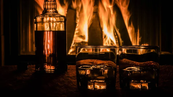 Gros plan de deux verres et une bouteille de whisky debout sur la table sur le fond d'une cheminée chaude — Photo