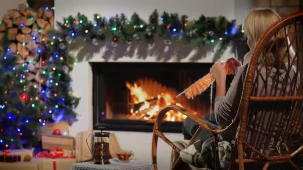 Back view of a woman knits while sitting by a fireplace decorated for Christmas — Stock Video