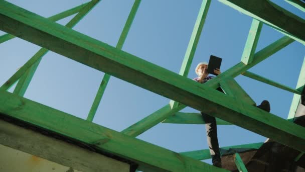 Une femme architecte travaille avec une tablette parmi les chevrons du toit. Supervision architecturale dans la construction — Video