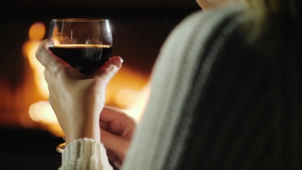 Hand med ett glas vin av en kvinna som kopplar av vid öppna spisen — Stockvideo