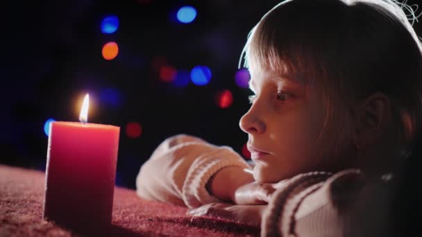 Una ragazza guarda una candela accesa, si siede sullo sfondo dell'albero di Capodanno la sera — Video Stock