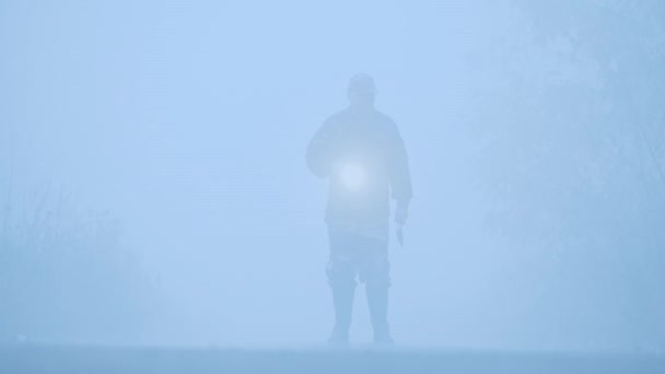 Илуэт человека с фонариком и топором, ходящим в тумане — стоковое видео
