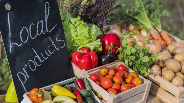 Counter with fresh vegetables and a sign of local products — Stock Photo, Image