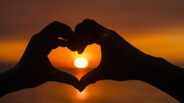 İki el, gökyüzünün ve güneşin görülebileceği bir kalp şekli oluşturur.