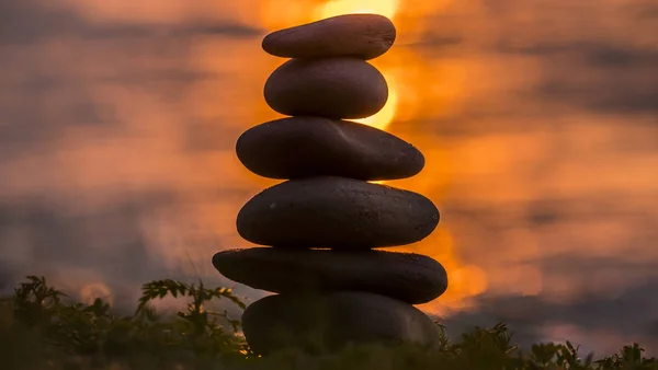 Pyramide de cailloux sur fond d'eau et de soleil couchant — Photo