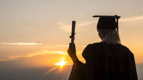 Laureato con diploma si trova sulla spiaggia, il sole illumina la mano con un diploma — Foto Stock