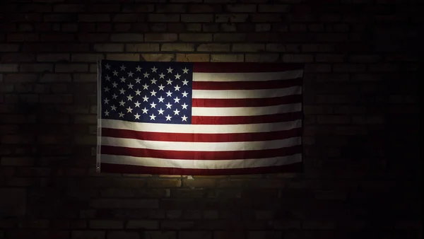 Amerikanische Flagge im Scheinwerferlicht hängt an Ziegelwand — Stockfoto