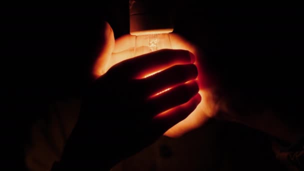 Een man houdt zijn handen om een elektrische gloeilamp. — Stockvideo