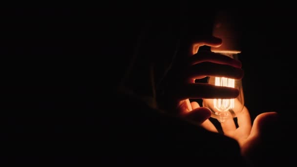 Vue arrière de l'homme réchauffe ses mains près d'une ampoule dans l'obscurité — Video