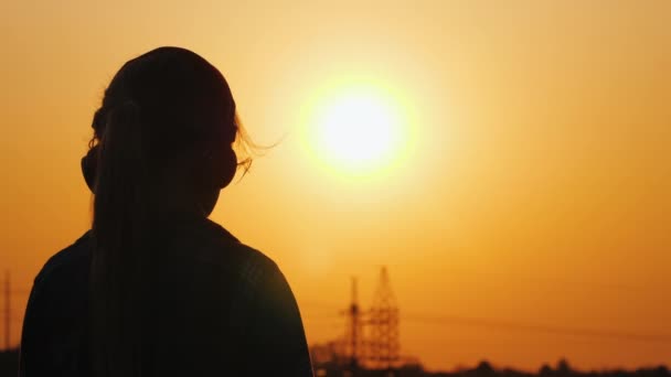 Uma criança em fones de ouvido ouvindo música no fundo do pôr do sol sobre a cidade — Vídeo de Stock