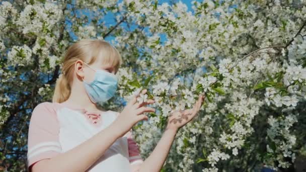 Ein Kinderallergiker in Maske bewundert die Blumen am Baum — Stockvideo