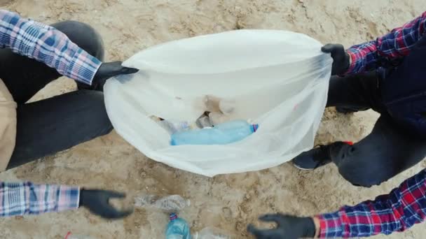 Voluntários colocam lixo plástico em um saco. Limpar a praia, cuidar do meio ambiente. Vista superior — Vídeo de Stock