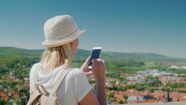 Una mujer usa un teléfono inteligente mientras viaja por Europa. Se encuentra en el fondo de una hermosa ciudad en Alemania. Vista trasera — Vídeos de Stock