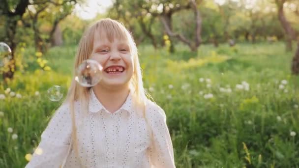 Glückliches blondes Mädchen, das mit Seifenblasen spielt. Lustig fängt sie ein — Stockvideo