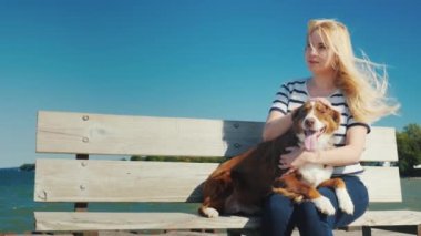 Köpekli bir kadın deniz kenarındaki bir bankta dinleniyor. Rüzgâr saçlarını karıştırıyor