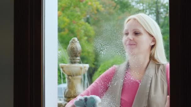 Une femme frotte une fenêtre dans un café ou un petit magasin. Vue de l'intérieur de la chambre — Video