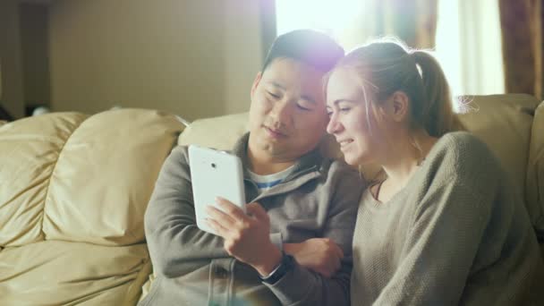 Junge multiethnische Paare verwenden gemeinsam ein Tablet. neben dem Sofa in Ihrem gemütlichen Zuhause sitzen — Stockvideo