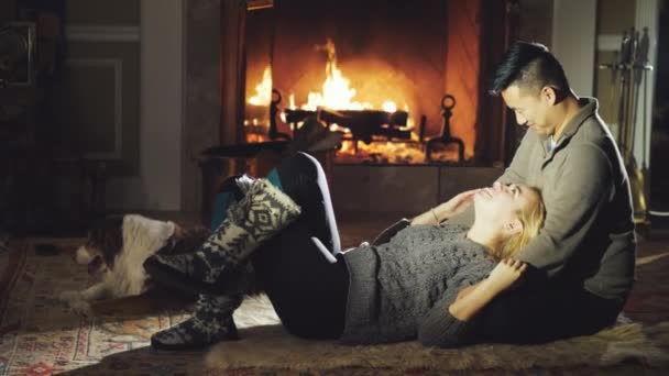 Una joven pareja multirracial está descansando junto al fuego, junto a su perro — Vídeo de stock