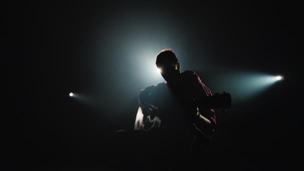 Un joven músico toca la guitarra en el escenario en el centro de atención — Vídeos de Stock