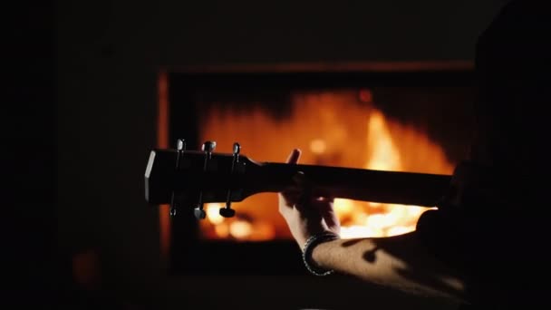 ミュージシャンはギターネック、クローズアップを手にします。暖炉のそばで遊ぶ — ストック動画