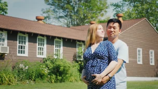 Familia joven y feliz cerca de su nuevo hogar. Mujer embarazada y hombre asiático — Vídeos de Stock